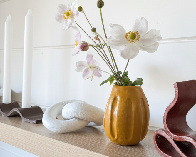 Yellow vase with flowers on a wooden shelf with decorative items