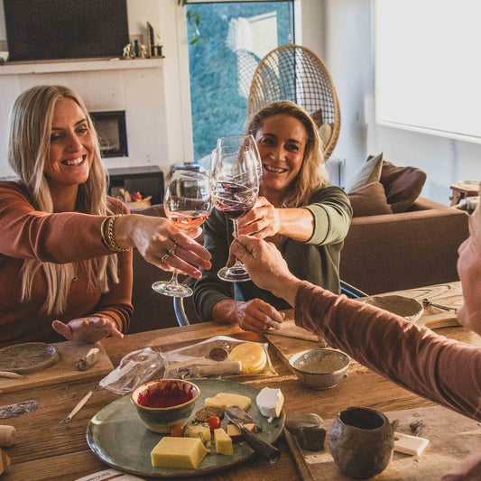 Three women toasting with wine glasses creating with clay in a cozy living room.