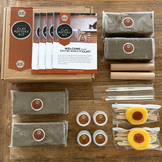 Clay pottery kit with packaging, clay blocks, tools, and instructions on a wooden surface.