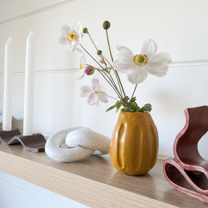 Yellow vase with flowers on a wooden shelf with decorative items