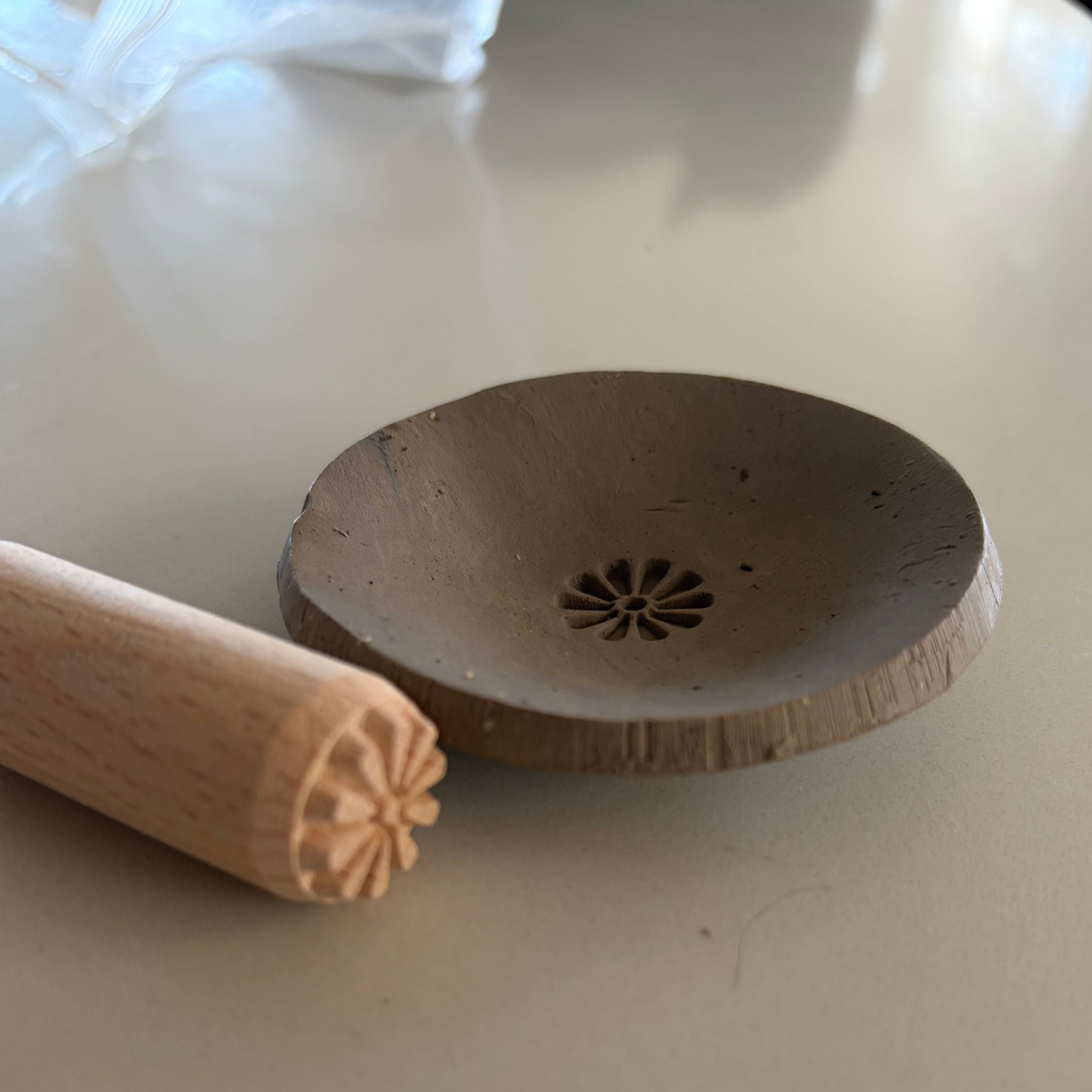 Wooden clay stamp next to pottery dish