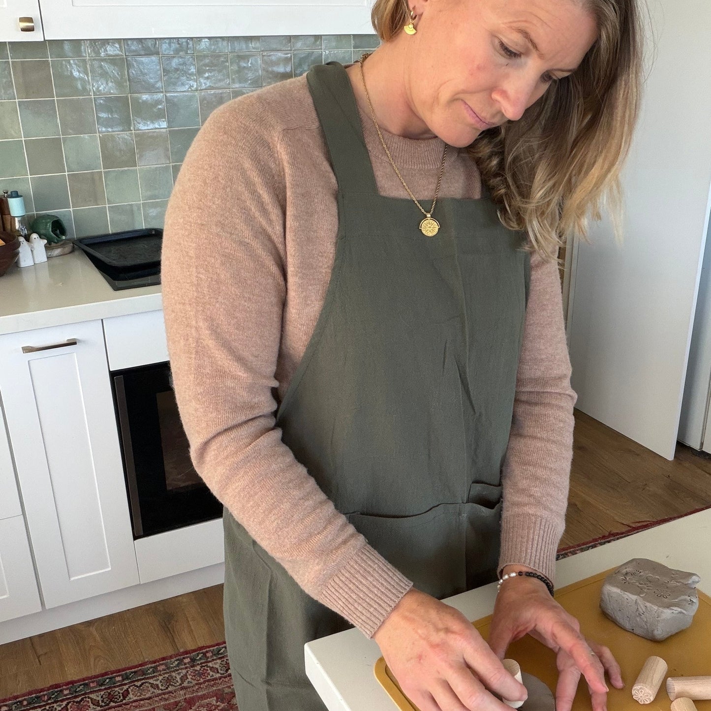 Woman in a kitchen wearing an apron, working with clay