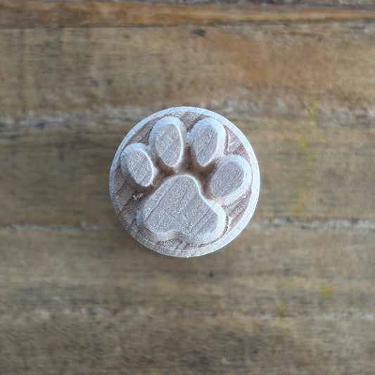 A round wooden stamp featuring an embossed paw print design, shown on a rustic wooden surface.